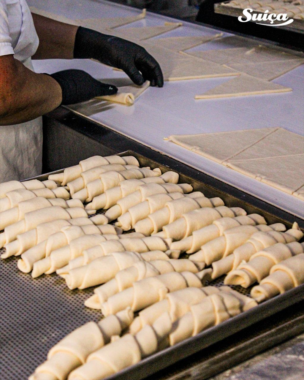 Bandeja cheia de croissants crus enfileirados, prontos para o forno.
